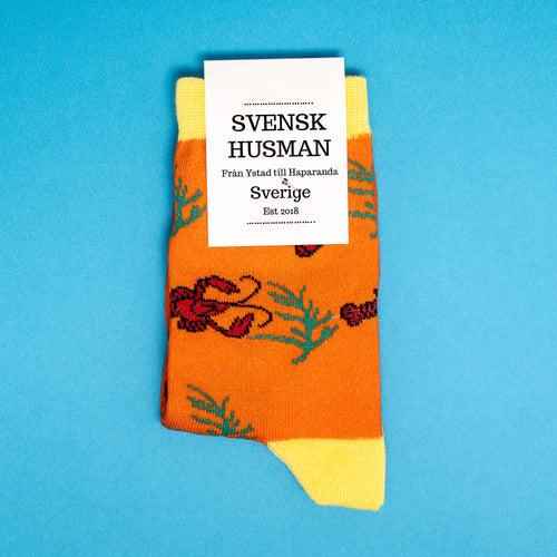 Orange barnstrumpor med mönster av röda kräftor och dillkvistar från Svenskhusman på blå bakgrund.