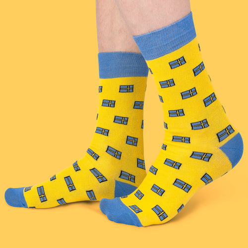 Gula strumpor från Svenskhusman med mönster av svenska flaggor och blå detaljer mot en gul bakgrund.