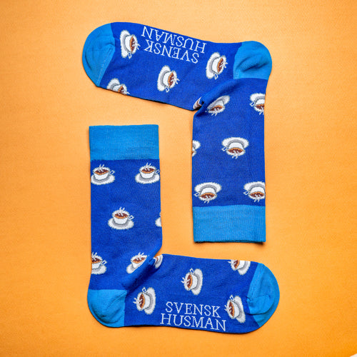 Blå mönstrade strumpor med vita kaffekoppar mot en orange bakgrund från Svenskhusman.