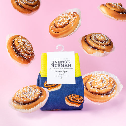 Blå og gule sokker med kanelbolle-mønster omgivet af svævende kanelboller på en lyserød baggrund.