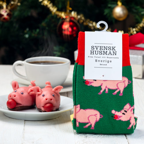 Gröna julstrumpor med mönster av julgrisar bredvid marsipangrisar och kaffe från Svenskhusman.